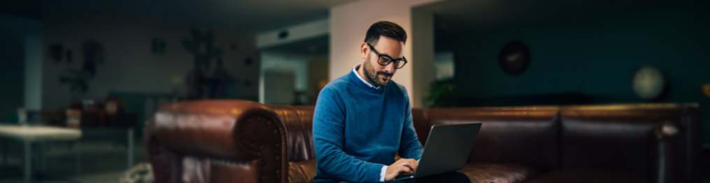 Hombre sentado en un sillón con su computadora apoyada en las piernas.